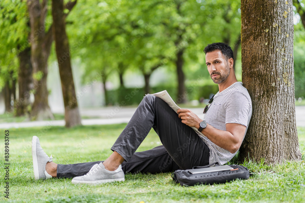 Man leaning against a tree in park reading newspaper Man leaning against a tree in park reading newspaper