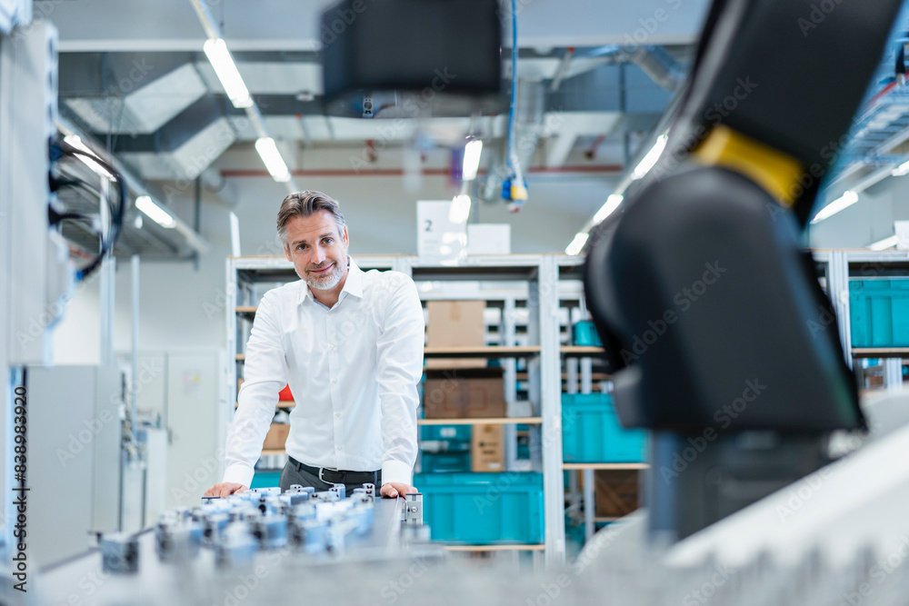 Confident businessman in a modern factory hall looking at robot