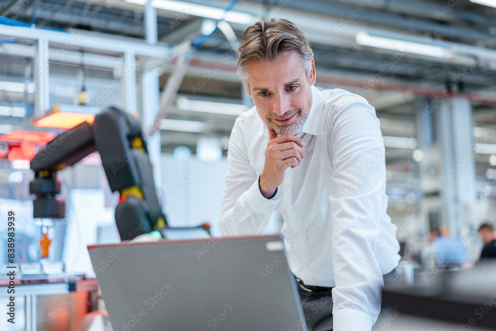 Confident businessman in a modern factory hall using laptop