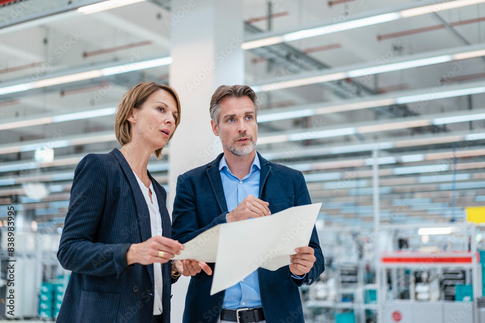Businessman and businesswoman discussing plan in a factory hall