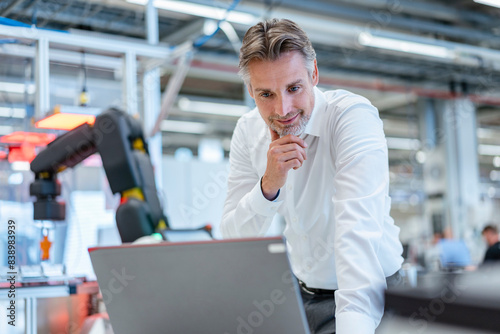 Obraz na płótnie Confident businessman in a modern factory hall using laptop w salonie