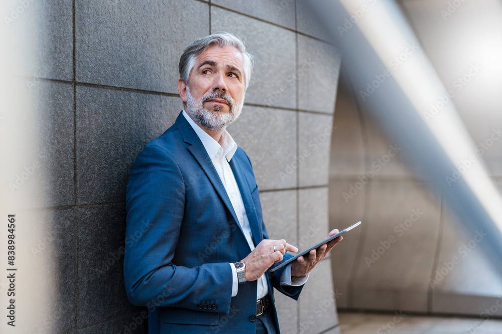 Mature businessman standing at a wall using tablet