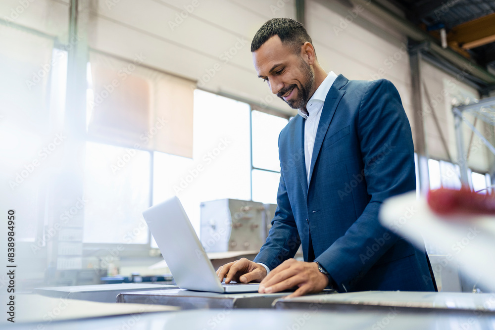 Smiling businessman using laptop in a factory Smiling businessman using laptop in a factory