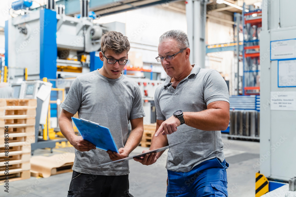 Male coworkers examining product while standing at illuminated factory