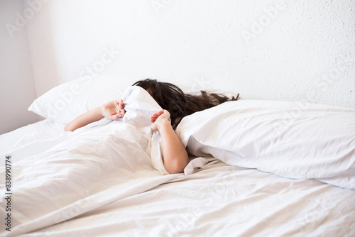 Girl lying in bed covering her face with blanket