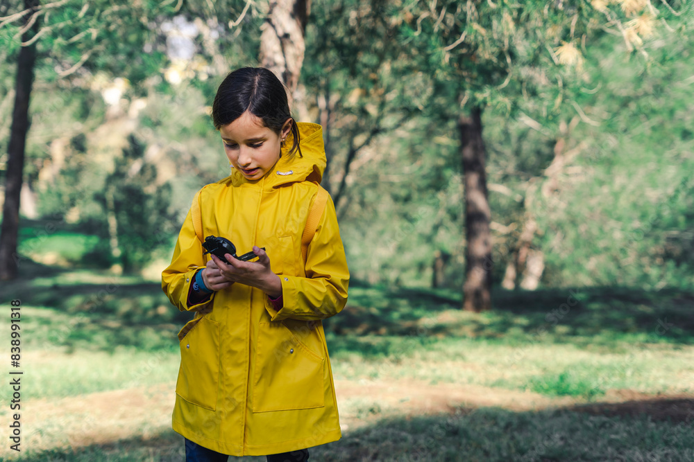 Girl wearing yellow raincoat in nature looking at compass Girl wearing yellow raincoat in nature looking at compass
