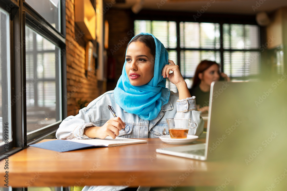 Businesswoman wearing turquoise hijab in a cafe and writing in notebook Businesswoman wearing turquoise hijab in a cafe and writing in notebook
