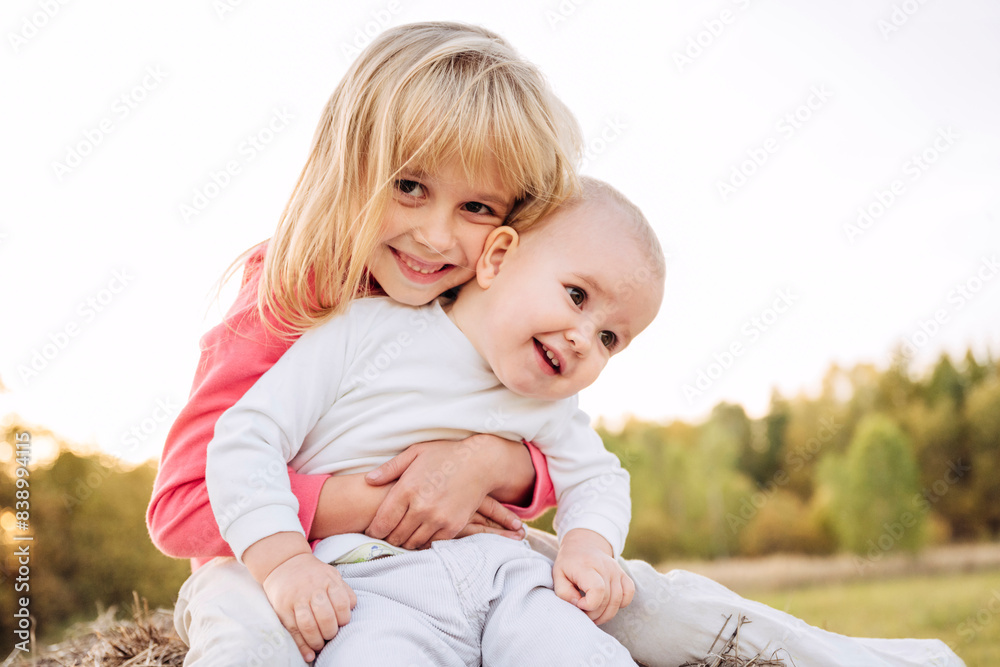Fototapeta premium Sister embracing female toddler against clear sky
