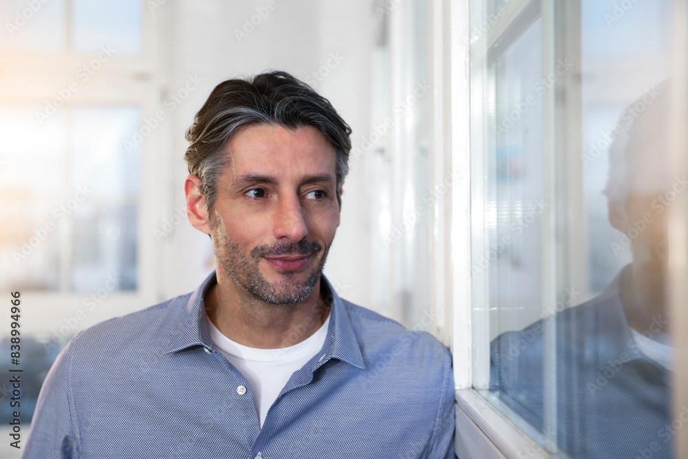 Smiling man in office looking out of window Smiling man in office looking out of window