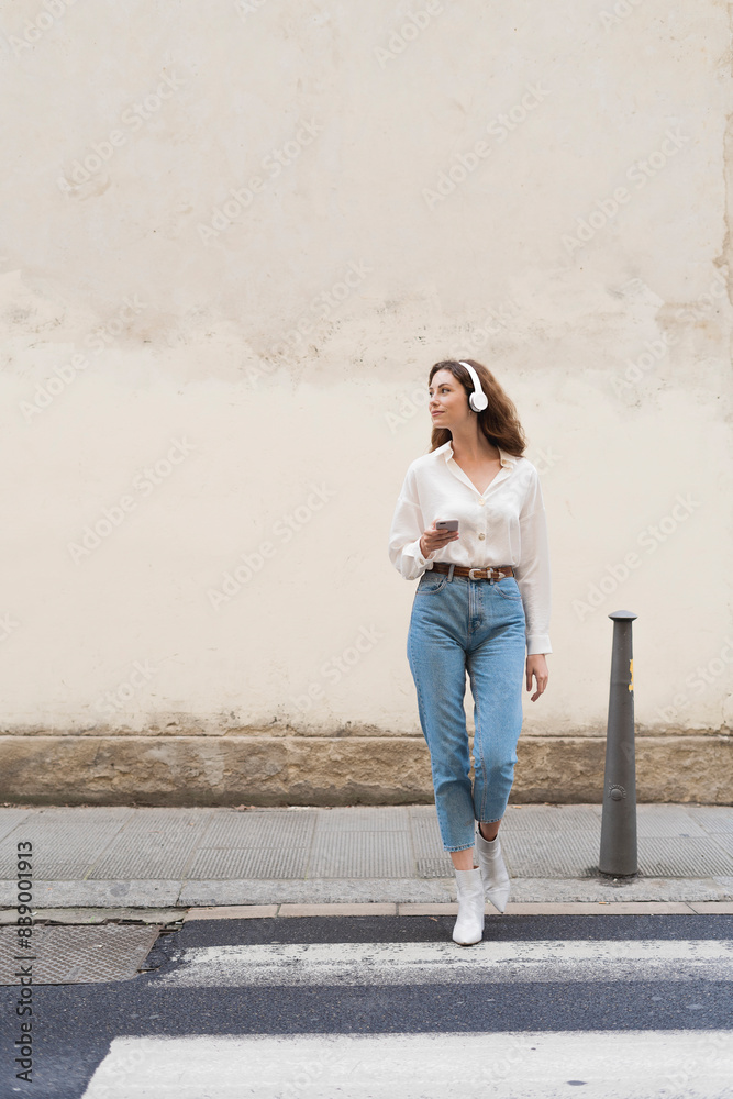 Young woman with smartphone and headphones crossing the street Young woman with smartphone and headphones crossing the street