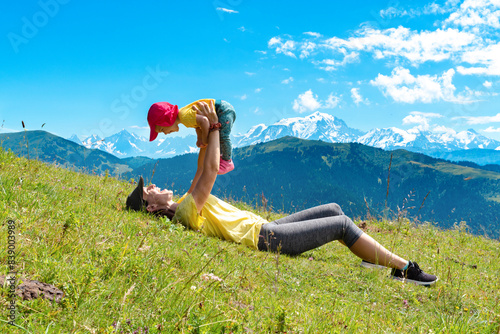 Mother picking up baby girl while lying on grass at Col des Aravis, Haute-Savoie, France photo