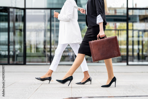 Obraz na płótnie Businesswoman with briefcase using mobile phone while walking by colleague on footpath w salonie