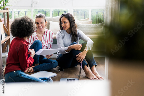 Three women with laptop and documents sitting on the floor at home photo