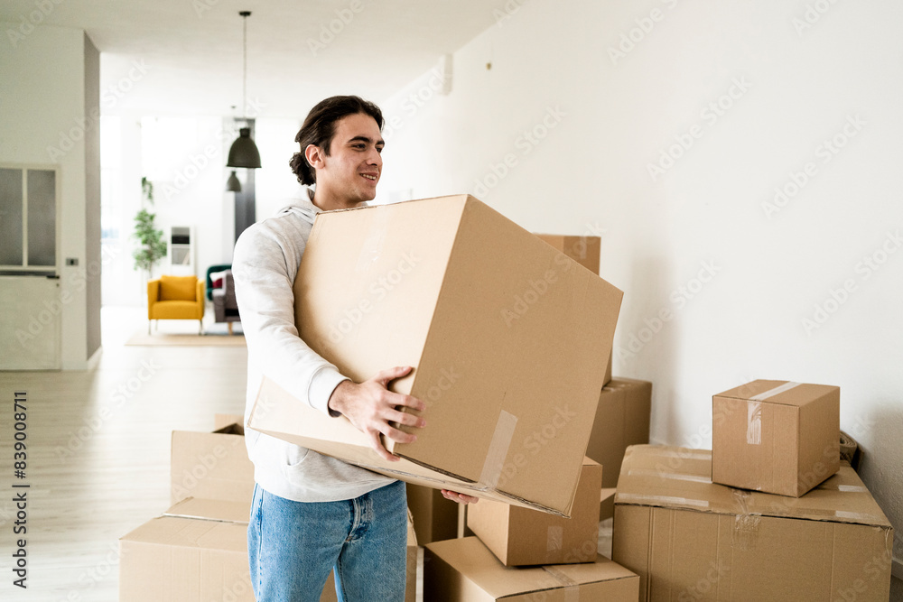 Smiling young man carrying cardboard box while moving in new apartment Smiling young man carrying cardboard box while moving in new apartment