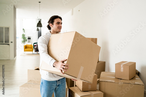 Smiling young man carrying cardboard box while moving in new apartment