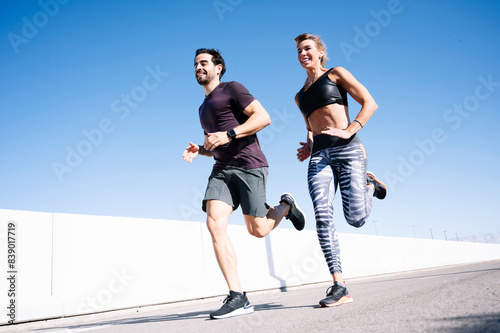 Smiling couple running on street against clear blue sky in city during summer photo