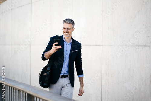 Smiling gray-haired businessman walking in the city using cell phone