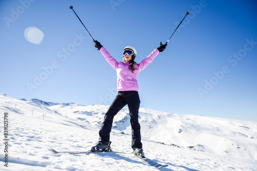 Happy woman raising her ski poles in snow-covered landscape in Sierra Nevada, Andalusia, Spain