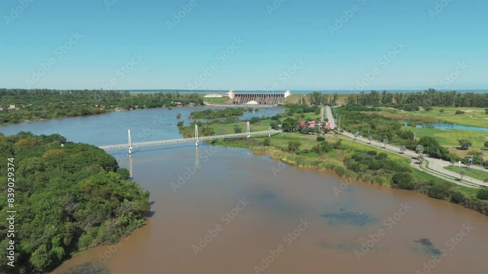 A stunning aerial image featuring a bridge with the Frontal Dam of Río Hondo in the background, set against the backdrop of a beautiful sunny day.