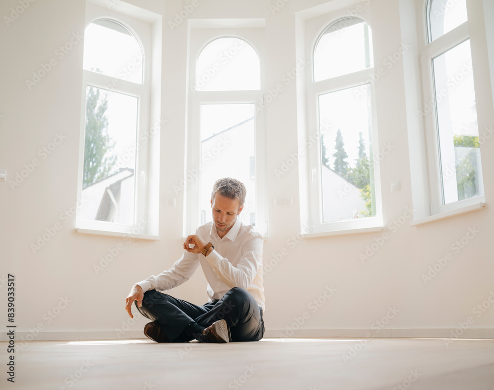 Businessman sitting on ground of his newly refurbished home, checking time Businessman sitting on ground of his newly refurbished home, checking time