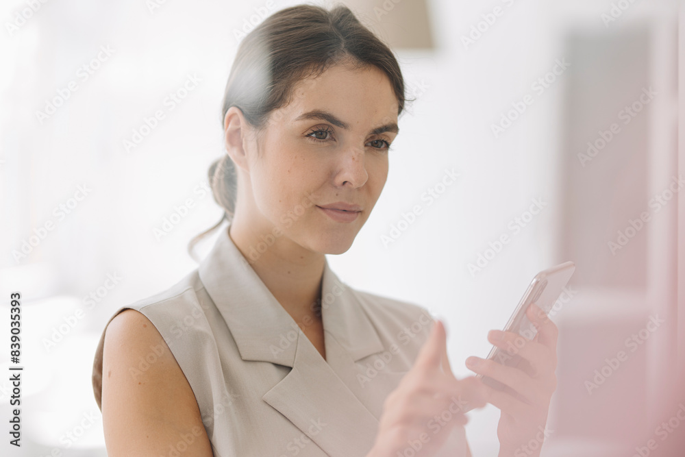 Woman pointing at glass wall while using mobile phone at office Woman pointing at glass wall while using mobile phone at office