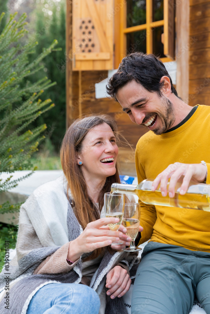 Happy man pouring wine in glass held by girlfriend while sitting outdoors Happy man pouring wine in glass held by girlfriend while sitting outdoors