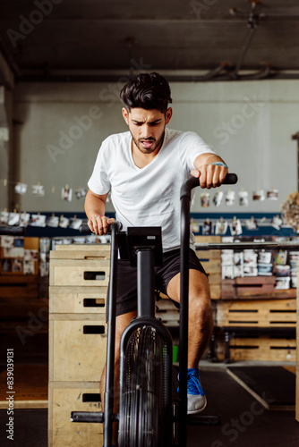 Young sportsman exercising on airbike at gym