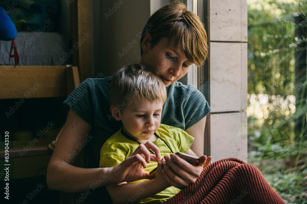 Mother and little son cuddling at home looking at smartphone