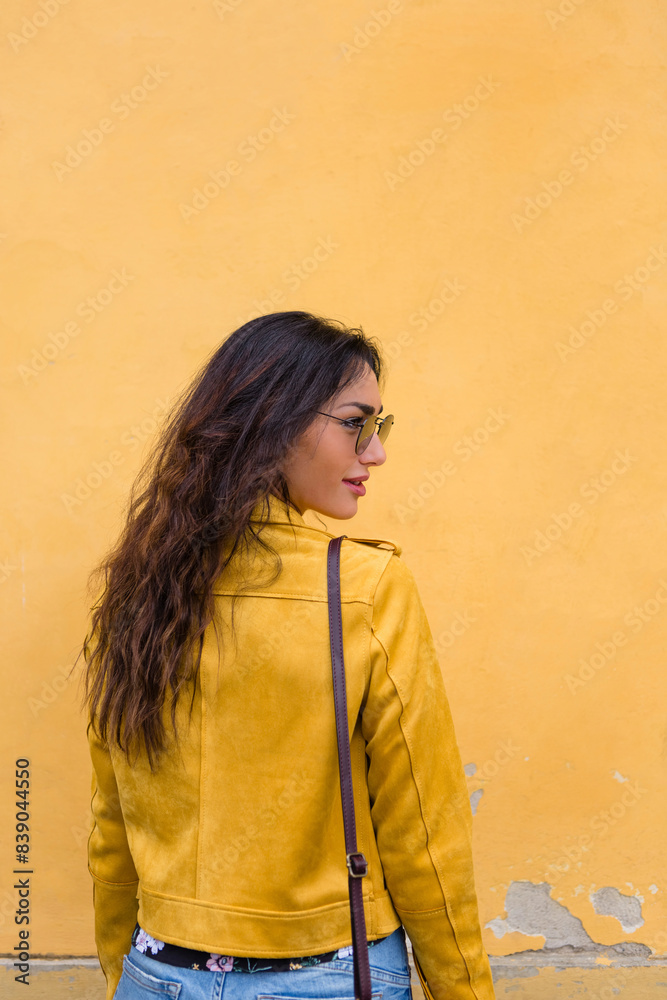 Portrait of young woman wearing yellow leather jacket and sun glasses, rear view Portrait of young woman wearing yellow leather jacket and sun glasses, rear view