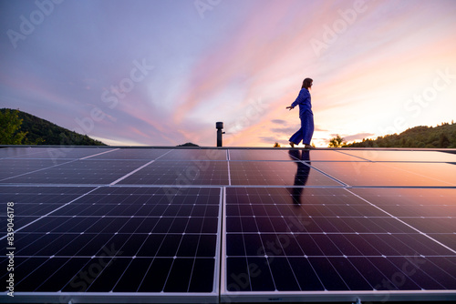 Rooftop with solar panels on house in mountains, woman walks alone enjoying sunset. Energy independence, sustainability, self sufficient, and escapism to nature concept