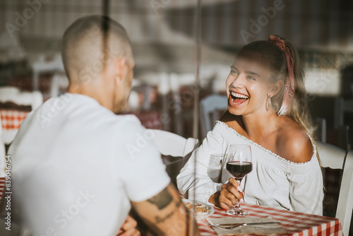 Happy woman holding wineglass looking at boyfriend in restaurant seen through window photo