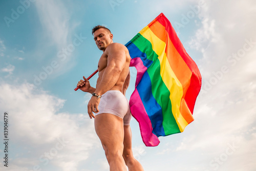 Obraz na płótnie Shirtless young man holding rainbow flag while standing against sky w salonie