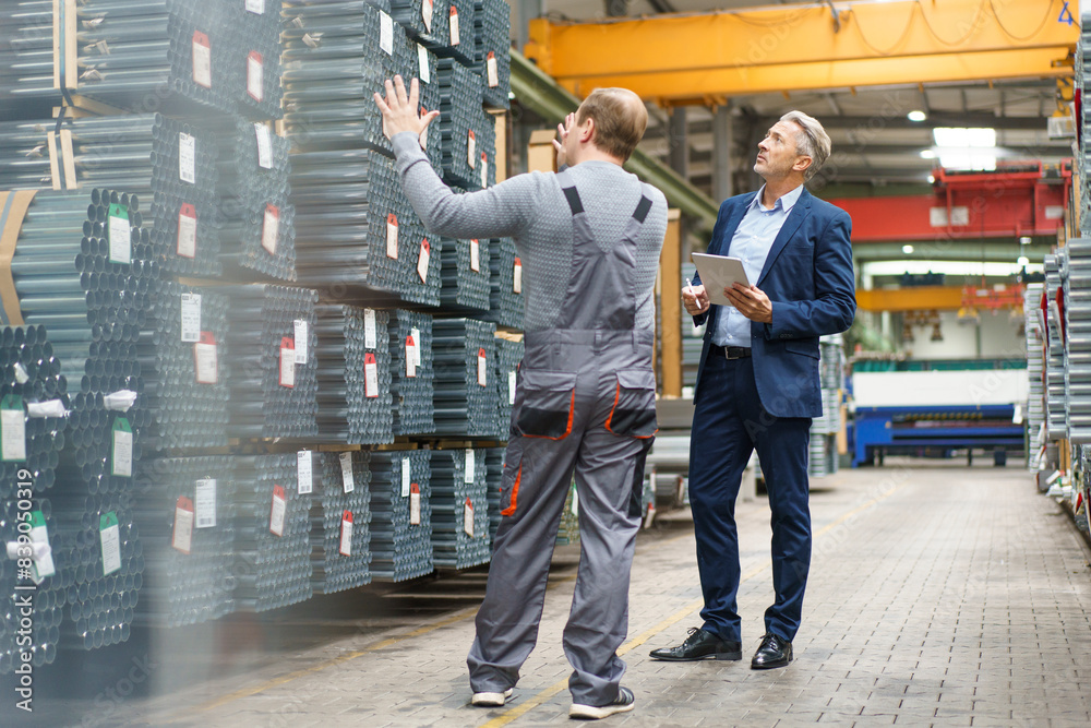 Businessman and worker talking in a factory storehouse