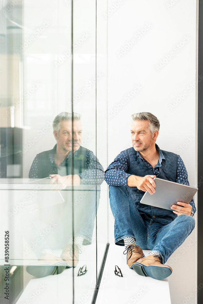 casual businessman sitting on windowsill in office building, using laptp casual businessman sitting on windowsill in office building, using laptp