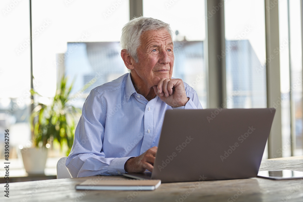 Portrait of pensive senior man sitting at table with laptop looking at distance Portrait of pensive senior man sitting at table with laptop looking at distance