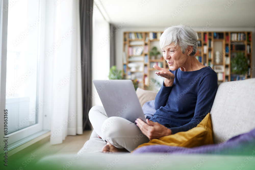 Senior woman giving flying kiss on video call while sitting at home Senior woman giving flying kiss on video call while sitting at home
