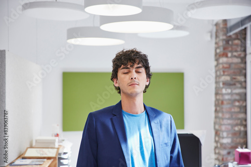 younh man standing in office with eyes closed photo