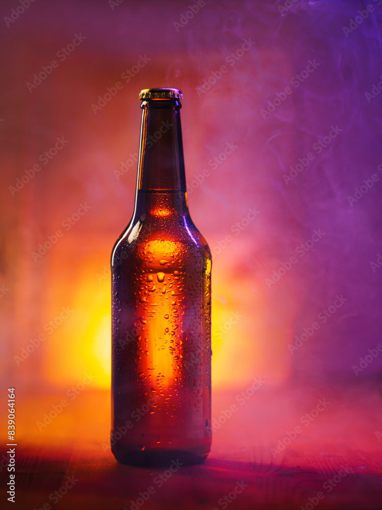 A bottle of cold beer in drops on a dark wooden background with colored light A bottle of cold beer in drops on a dark wooden background with colored light