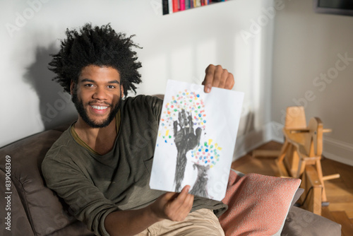 Man sitting on couch in living room showing children's drawing