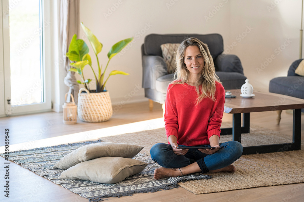 Portrait of smiling woman sitting on the floor at home holding tablet Portrait of smiling woman sitting on the floor at home holding tablet