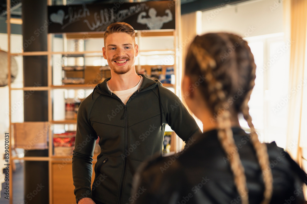 Coach talking to young woman at front desk of a gym