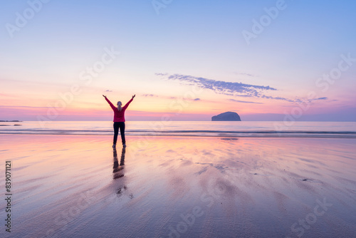 Mature woman with arms raised standing at Seacliff Beach during sunset, North Berwick, Scotland photo