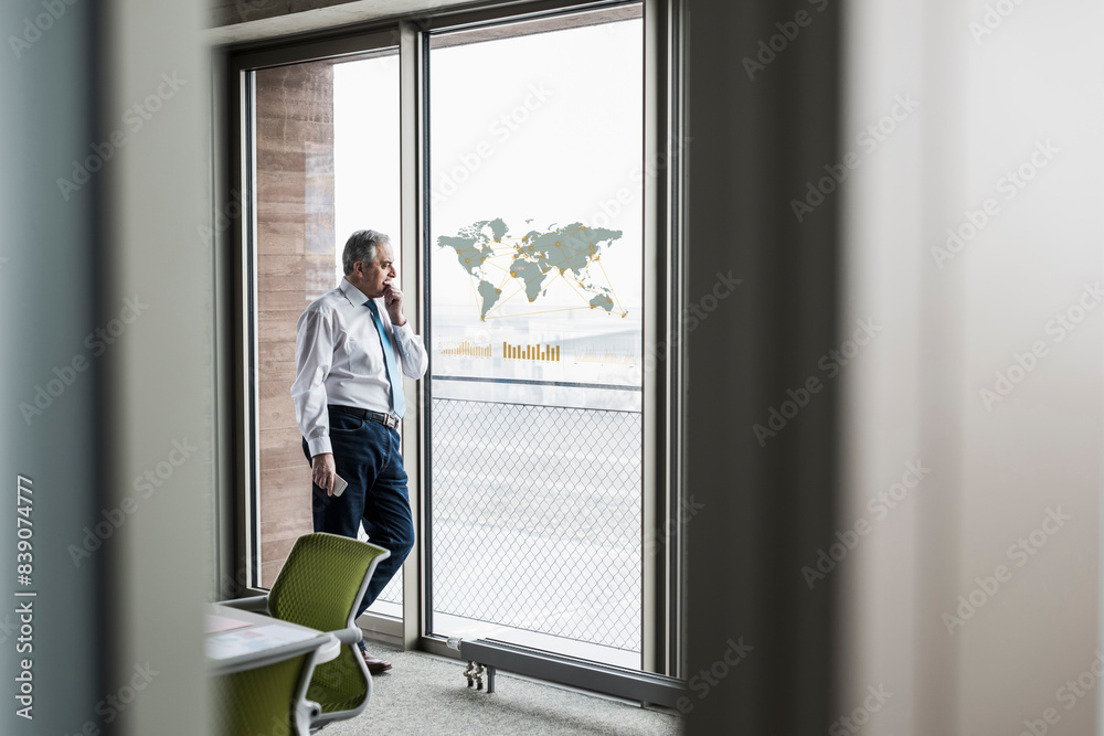 Businessman looking at windowpane with world map in office Businessman looking at windowpane with world map in office