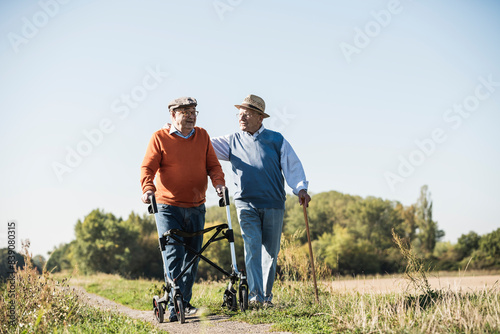 Old friends taking a stroll in the fields with walking stick and wheeled walker, talking about old times