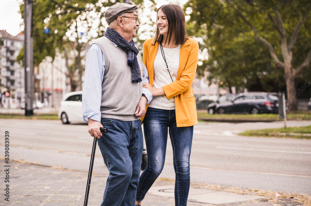 Adult granddaughter assisting her grandfather strolling with walking stick