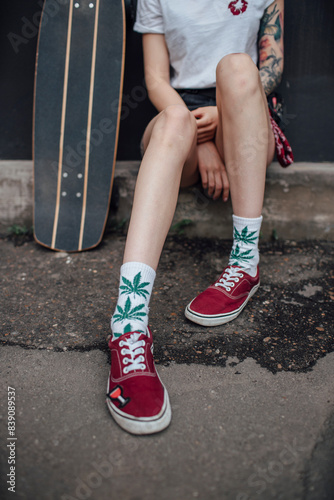Woman's legs in socks and sneakers sitting next to carver skateboard