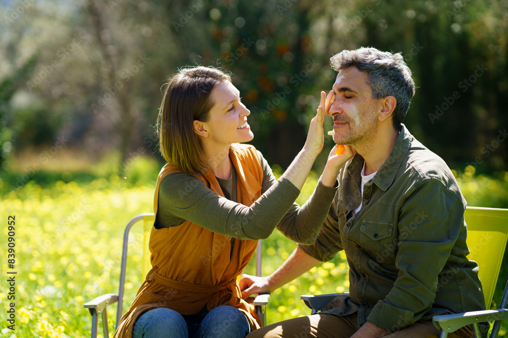 Young woman putting sunscreen on her boyfriend in the field