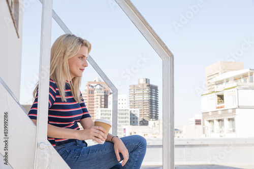 Young woman drinking coffee, sitting on stairs on a rooftop terrace © tunedin