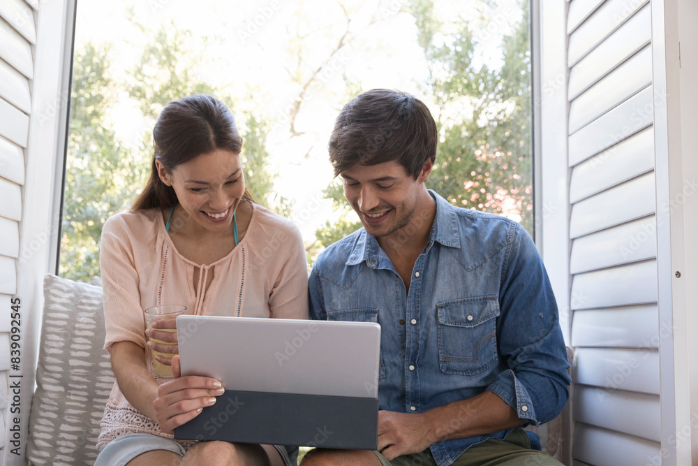 Smiling young couple sitting on windowsill sharing tablet Smiling young couple sitting on windowsill sharing tablet