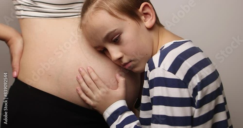 Little boy looking at her mother pregnant tummy. Pregnant mother and son spending time together at home.